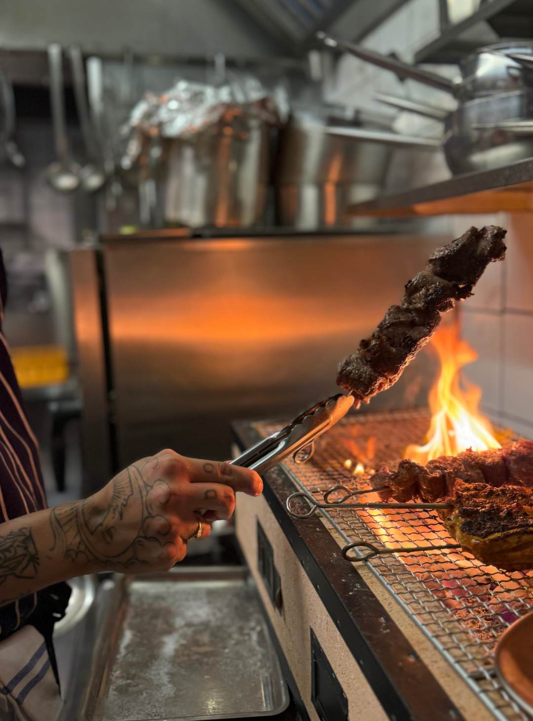 Kock som lyfter ett färdiggrillat spett från kolgrillen med tång.